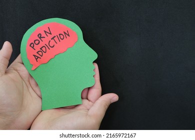 Porn addiction treatment and how to deal with concept. Hand holding human head profile with pornography word on brain.