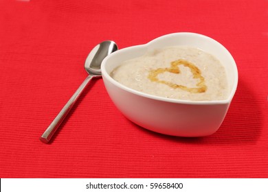 porridge in a heart shape bowl on red canvas background with honey