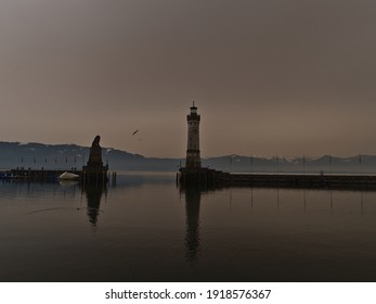 Port basin of Lindau, Lake Constance, Germany with lighthouse and lion sculpture on winter day. Orange colored sky due to rare weather phenomenon, when desert sand particles of Sahara are in the air. - Powered by Shutterstock