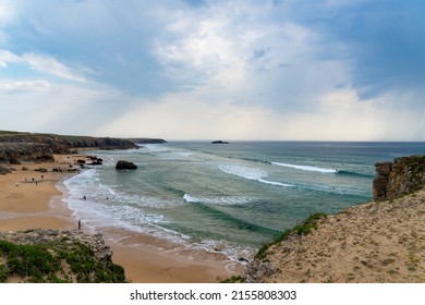 Port Blanc Beach On The Quiberon Peninsula, Bordered By Cliffs, Emerald Coloured Waves And White Foam. Surfers In The Water And Walkers On The Sandy Beach. 