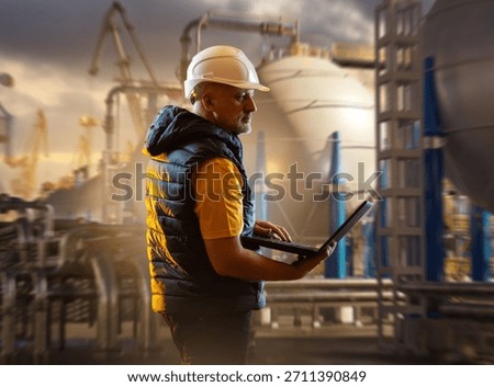 Port engineer supervises LNG loading operations, monitoring equipment and transfer systems on a laptop to ensure safe handling of liquefied gas during terminal procedures.
