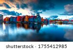 Port in Groningen in the Netherlands. Boats, houses and beautiful sky at sunrise reflected in the sea. There are dramatic clouds in the sky.