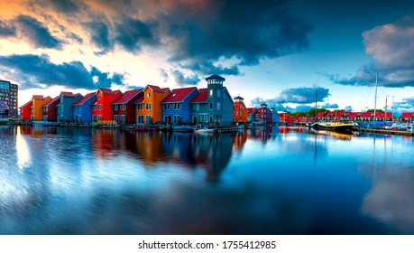 Port in Groningen in the Netherlands. Boats, houses and beautiful sky at sunrise reflected in the sea. There are dramatic clouds in the sky.