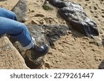 Port Louis, Bretagne, France : A girl sitting at the edge of an old dike with black boots in the air above the beach, blue jean, very sunny day