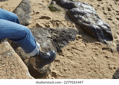 Port Louis, Bretagne, France : A girl sitting at the edge of an old dike with black boots in the air above the beach, blue jean, very sunny day - Powered by Shutterstock