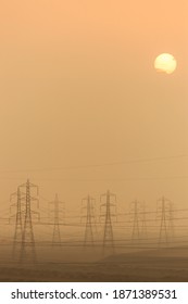 Port Said, Egypt, 11 05 15: View From The Suez Canal Of The Silhouette Of Electricity Pylons And Power Lines In A Desert Landscape Against An Eerie Orange Sandy Sky With A Visible Sun 