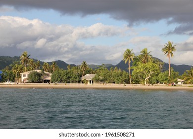 Port Vila, Vanuatu - January 20, 2013: Peaceful Sunday Afternoon In A Village, Locals Splashing Around In The Ocean In Front Of Their Huts, Coconut Palms Framing The Scene, Dark Clouds Above