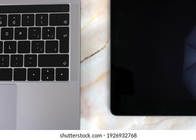 Portable computer next to a digital tablet on a pink marble background
