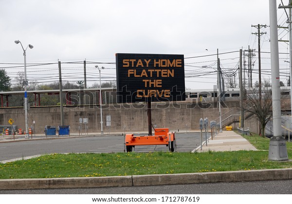 Portable digital electronic\
sign in a parking lot advising people to stay home to flatten the\
curve