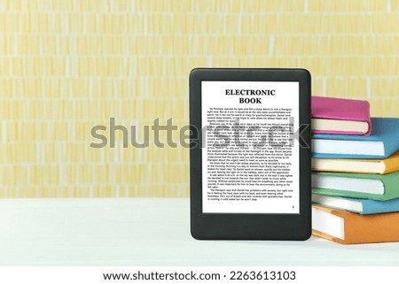 Portable e-book reader and stack of books on white wooden table, space for text