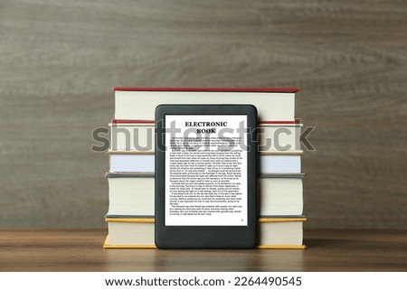 Portable e-book reader and stack of hardcover books on wooden table
