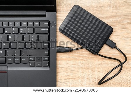 A portable hdd connected to a laptop on a wooden background, top view. The concept of data storage