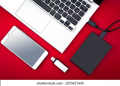A portable hdd connected to a laptop with usb flash drive and smartphone on a red background, flat lay. The concept of data storage