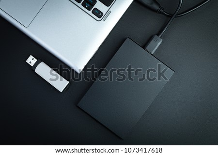 A portable hdd connected to a laptop with usb flash drive on a black table, flat lay. The concept of data storage