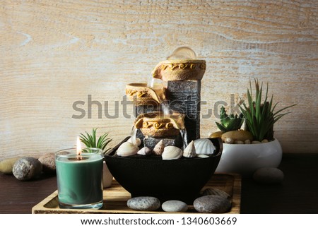 Portable indoor fountain for good Feng Shui in home or office. Small indoor tabletop fountain with water flowing. Spiritual mind and soul balance concept. Green plants in flower pot on background.