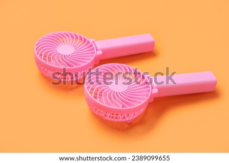 Portable pink electric fans on orange background, closeup