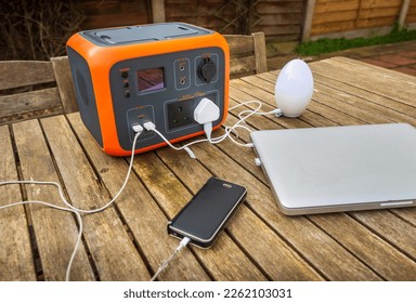 Portable power station solar electricity generator outdoors on wooden table with laptop, mobile phone and lamp electronic devices charging. Wireless charging lithium battery backup for use off grid. - Shutterstock ID 2262103031