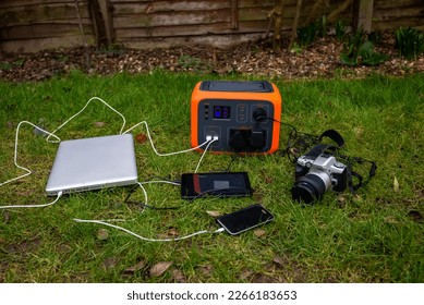 Portable power station solar electricity generator with laptop, tablet and camera electronic devices charging outdoors on garden lawn grass. Wireless charging lithium battery backup for use anywhere. - Shutterstock ID 2266183653