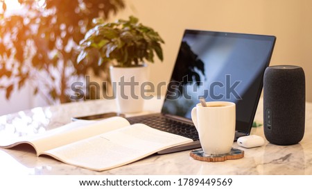 A portable speaker with built-in smart intelligence. Musical column. Marble table, work atmosphere, laptop, green flower, coffee cup. Morning sunlight.