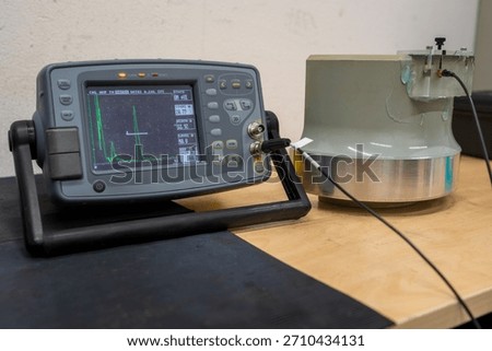 A portable ultrasonic testing device is undergoing a calibration procedure with a reference block showing signal amplitude peaks on the monitor for inspection of equipment accuracy