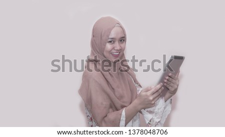 Portait of asian muslim woman wearing head scarf or hijab playing with tablet pc smiling at camera -image