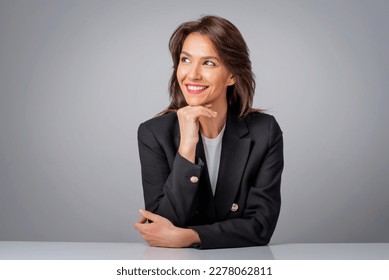 Portait of an attractive businesswoman looking up and cheerful smiling against isolated grey background. Brunette haired female wearing black blazer. Copy space.