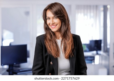 Portait of an attractive businesswoman sitting at the offiice. Mid aged professional woman wearing black blazer and looking at camera. 