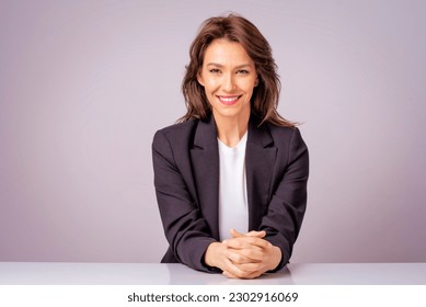 Portait of an attractive businesswoman wearing black blazer while sitting at isolated grey background. Copy space. 