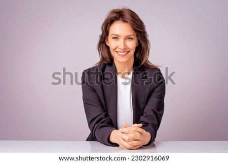 Portait of an attractive businesswoman wearing black blazer while sitting at isolated grey background. Copy space. 