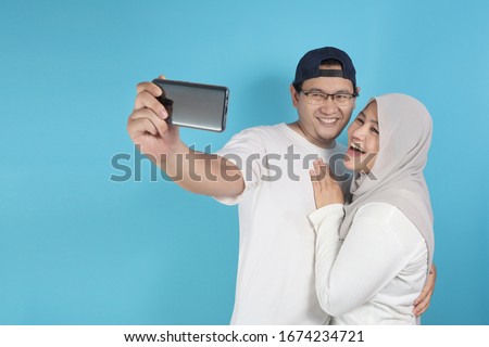 Portait of happy Asian muslim couple making selfie and smiling, husband and wife hugging full of love, family concept