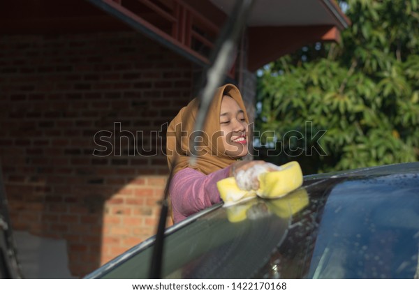 portait of hijab woman cleaning her car roof in\
front of her garage at outdoors area. Transportation self service,\
cleaning car concept.