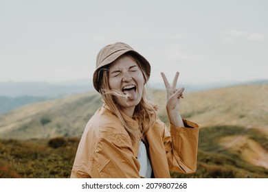 Portait of positive young blond woman having fun shows peace sign outdoors on the top of the mountain