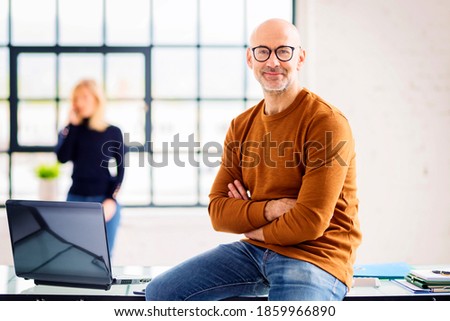 Portait shot of senior businessman wearing casual clothes while sitting at desk in the office.