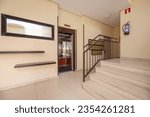 Portal of a residential housing building with polished light terrazzo tiles, a staircase with a brown metal railing and an elevator with mirrors and wood