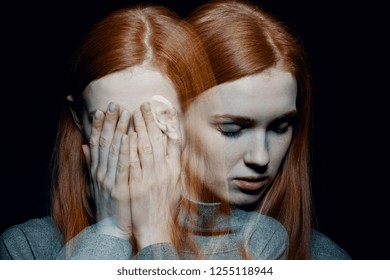 Porter of beautiful redhead girl with psychotic disorders covering her face, hiding from her hallucinations, black background behind her