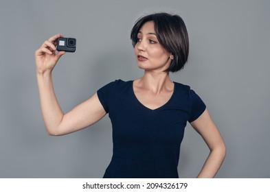 Porter of  woman with short black hair holding a camera with one hand. Head is turned to  side. Gopro. Action camera - Powered by Shutterstock