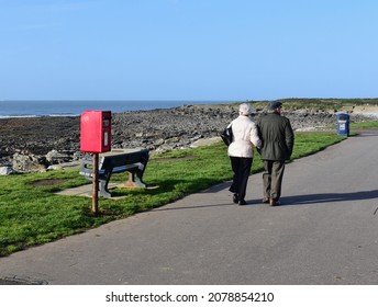 Porthcawl, Bridgend County Borough, Wales UK - 11.17.2021: A View Across The Rocky Foreshore And Beach At Porthcawl. Outcrops Of Rocks And Water Outlet Pipe In Distance. Older Couple Enjoying A Walk.