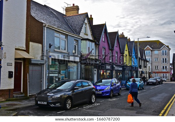 Porthcawl, County Borough of Bridgend / Wales UK -\
2/23/2020: A view along Well Street, a popular side street in the\
town centre, and home to shops, restaurants and offices. Woman\
crossing road.
