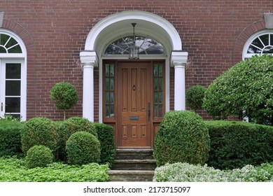 Portico Entrance Of Traditional Brick House Surrounded By Shrubbery, With Elegant Wood Grain Front Door With Sidelights