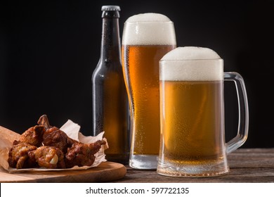 Portion of chicken meat for beer. Well-baked and juicy wings will serve a good addition to a glass of ale. Studio shot of food on black.
