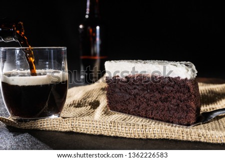 Portion of chocolate cake and black beer on black background wit
