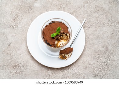 Portion of Classic tiramisu dessert in a glass cup on concrete background