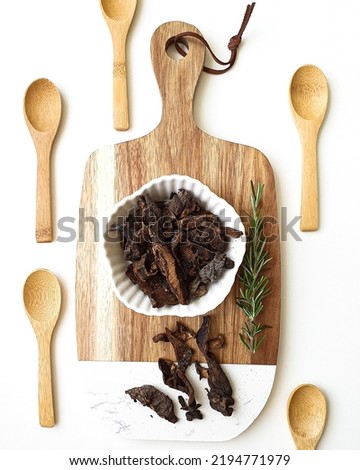 Portion of dried funghi mushroom on a wooden cutting board on a white background. Mini wooden spoons for decoration.