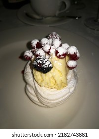 Portion Of Famous Pavlova Meringue-based Dessert With Whipped Cream And Berries In Blurry Background Of Tableware. This Dessert Is Originated In Australia Or New Zealand, Named After Ballerina Pavlova