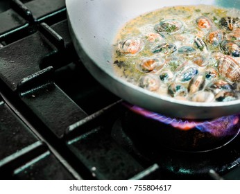 Portion Of Fresh Clams Bubbling In A Savory Sauce On A Gas Burner In A Restaurant In A Close Up Partial Overhead View Of The Pan With Copy Space