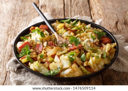 portion of fried cabbage with bacon closeup on a plate on a wooden table. horizontal
