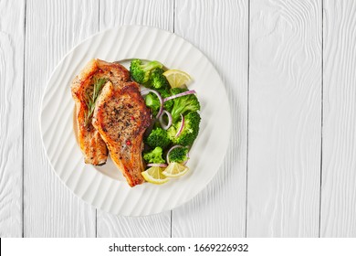 A Portion Of Fried Pork Rib Chops With Lemon Wedges, Broccoli Salad On A White Plate On A Wooden Table, Horizontal View From Above, Flat Lay, Free Space