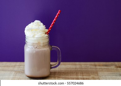 Portion of hot chocolate with white whipped cream in a glass jar with red paper straw, purple background, wooden table - Powered by Shutterstock