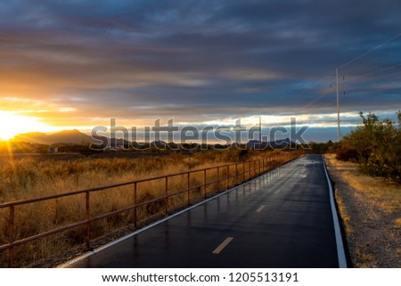 A portion of The Loop walking, biking, running and jogging path in Tucson, Arizona. A beautiful Sonoran Desert Sunset lights up the sky and the roadway wet with recent rain reflects the railing. 2018.