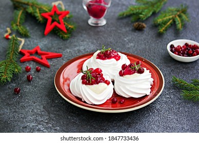 Portion Pavlova meringue pastries with cream and cranberry sauce in New Year's or Christmas decor on a red plate on a dark concrete background. New Year and Christmas desserts. Selective focus